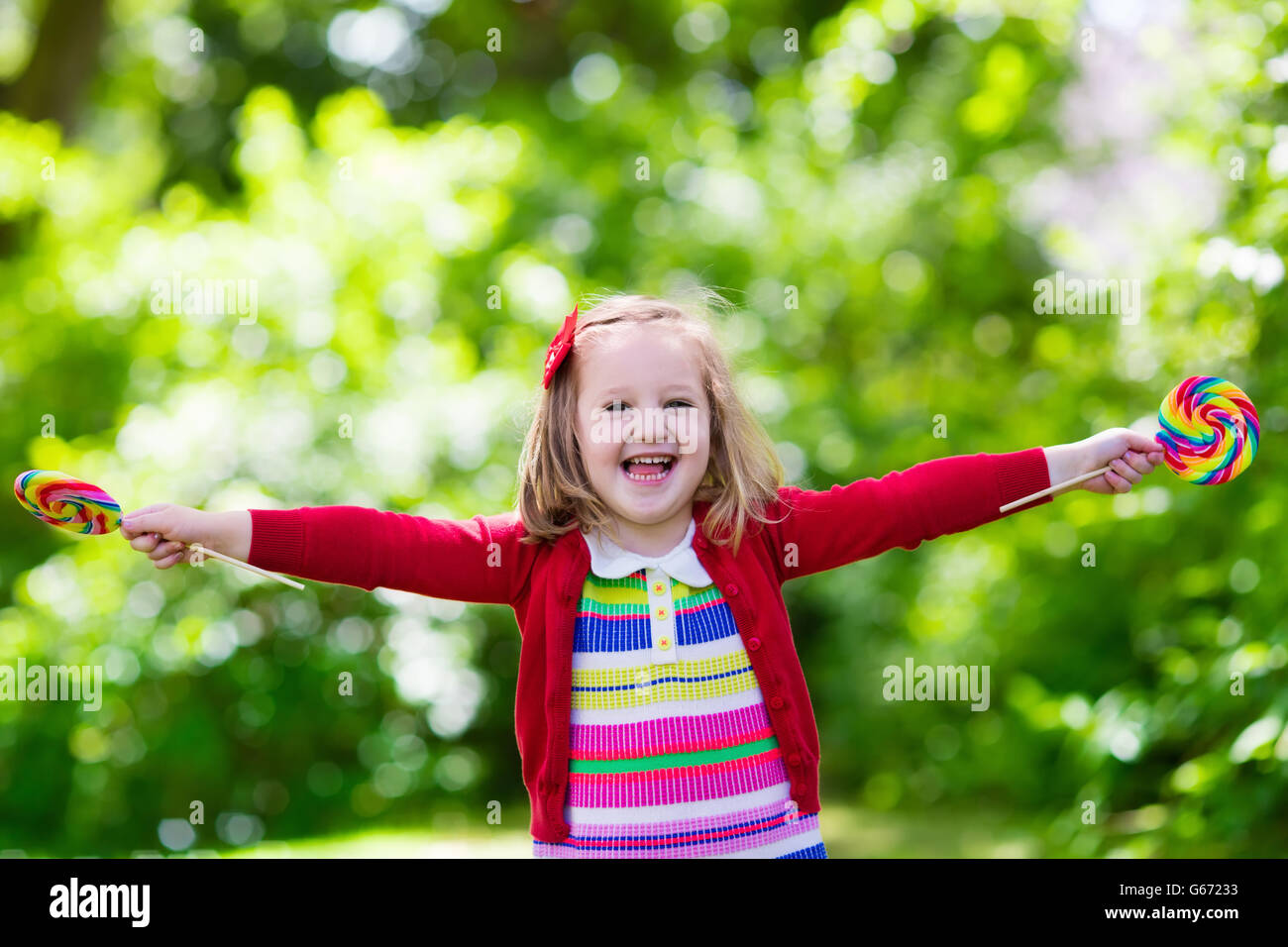 Cute little girl with big colorful lollipop. Child eating sweet candy bar. Sweets for young kids. Summer outdoor fun. Stock Photo