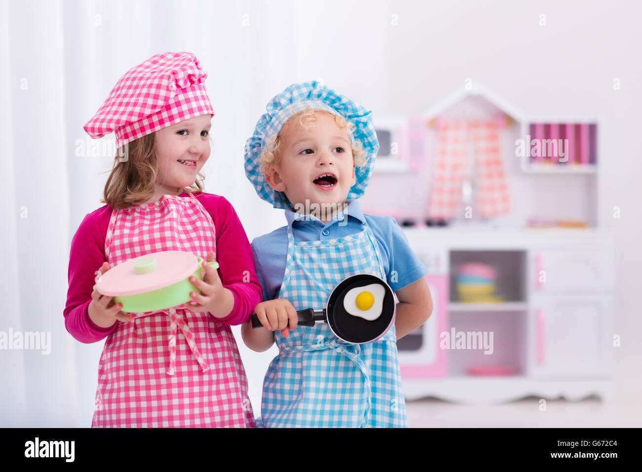 Little Girl And Boy In Chef Hat And Apron Cooking In Toy Kitchen