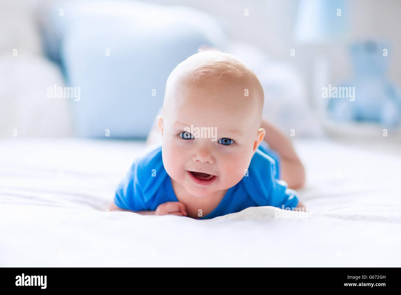 Adorable baby boy in white sunny bedroom. Newborn child relaxing in bed. Nursery for young