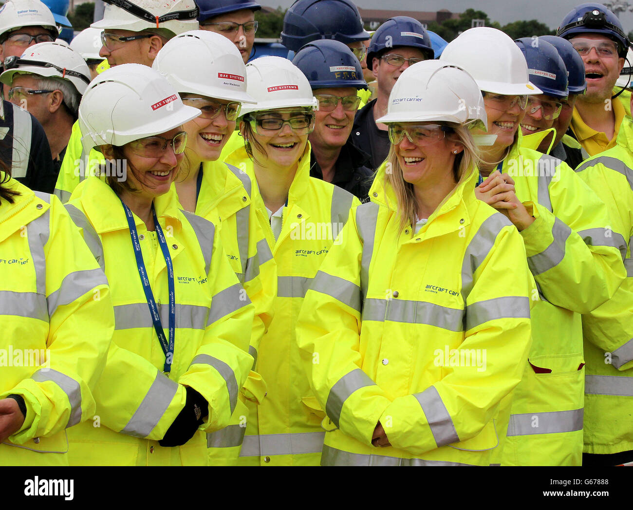 Workers watch a plaque with the emblems of the Royal Navy,The Royal Air Force and the British Army which will be embedded into the fabric of HMS Queen Elizabeth aircraft carrier after the AFT island was lowered into place at Babcock's Rosyth Dockyard. Stock Photo