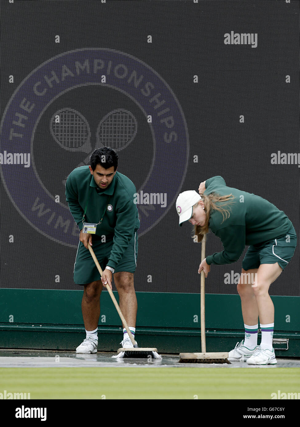 Ground staff sweep away rain water before the start of play during day five of the Wimbledon Championships at The All England Lawn Tennis and Croquet Club, Wimbledon. Stock Photo