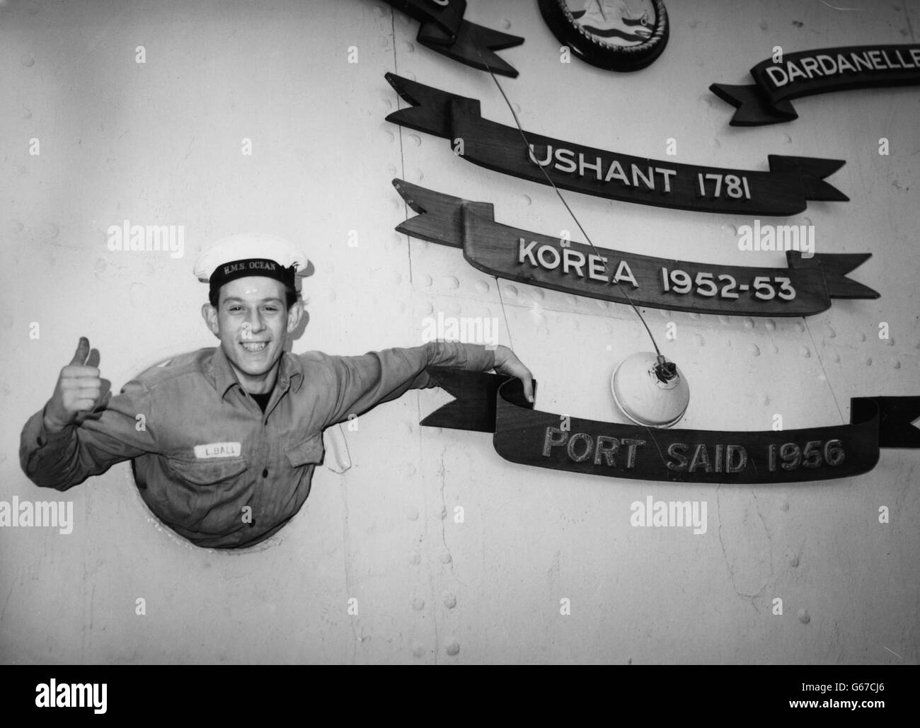 Junior Seaman Len Ball, 17, points to the name 'Port Said', the latest battle honour to be added to the Royal Navy's aircraft carrier Ocean, which arrived at Devonport from Egypt. Stock Photo