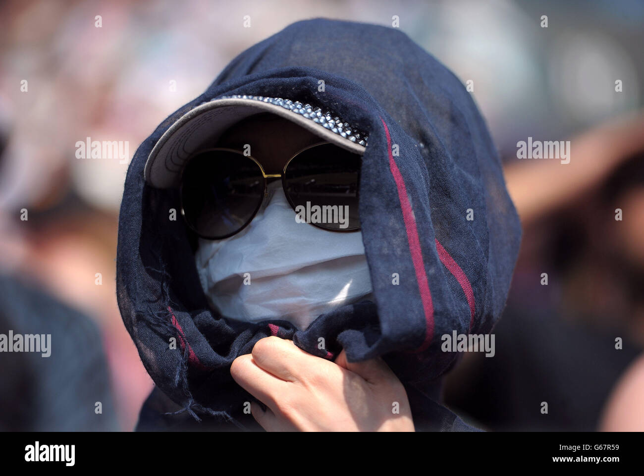 A spectator covers up to shield herself against the sun during day twelve of the Wimbledon Championships at The All England Lawn Tennis and Croquet Club, Wimbledon. Stock Photo