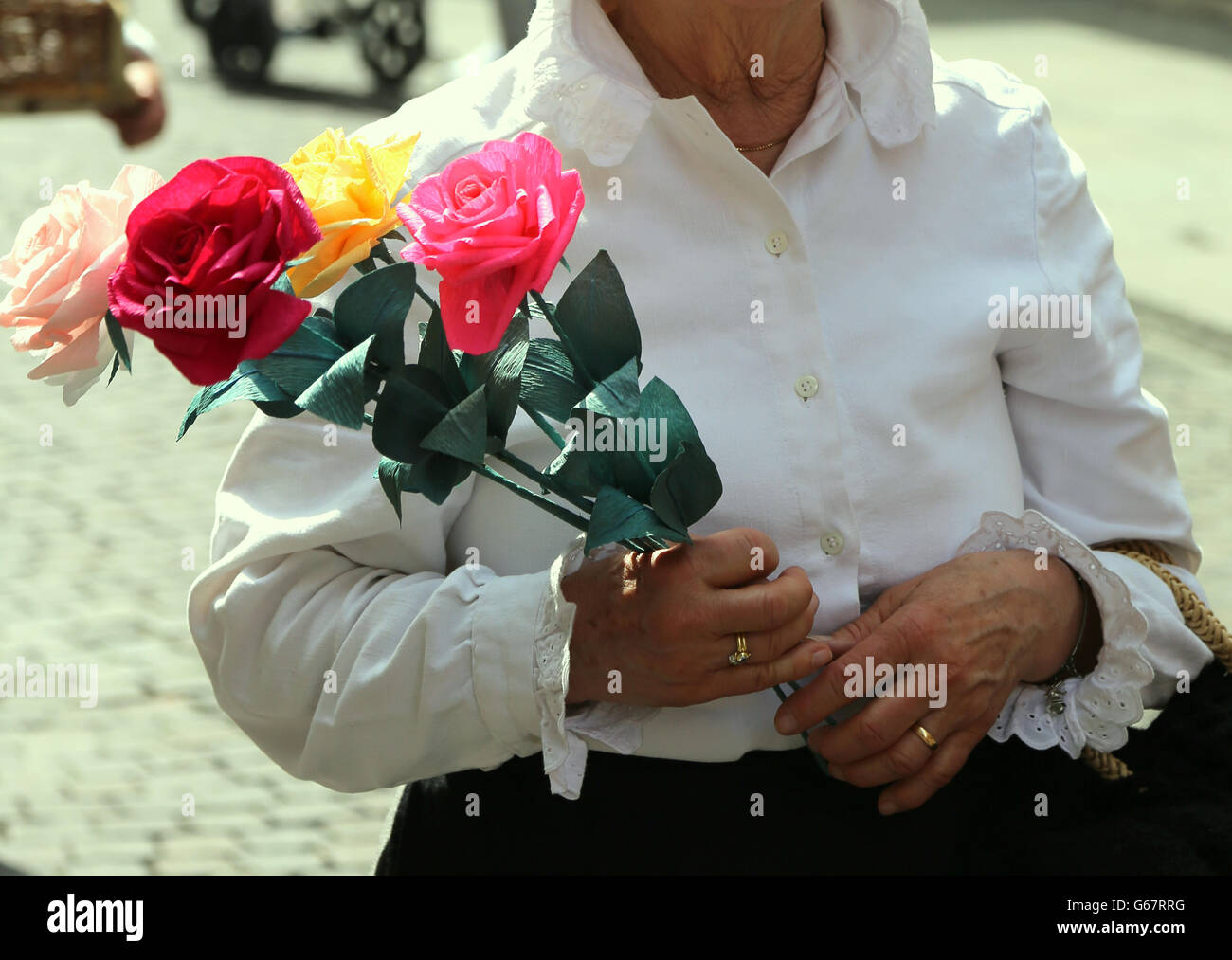 old lady with white blouse walks with a pack of four roses in her hand Stock Photo