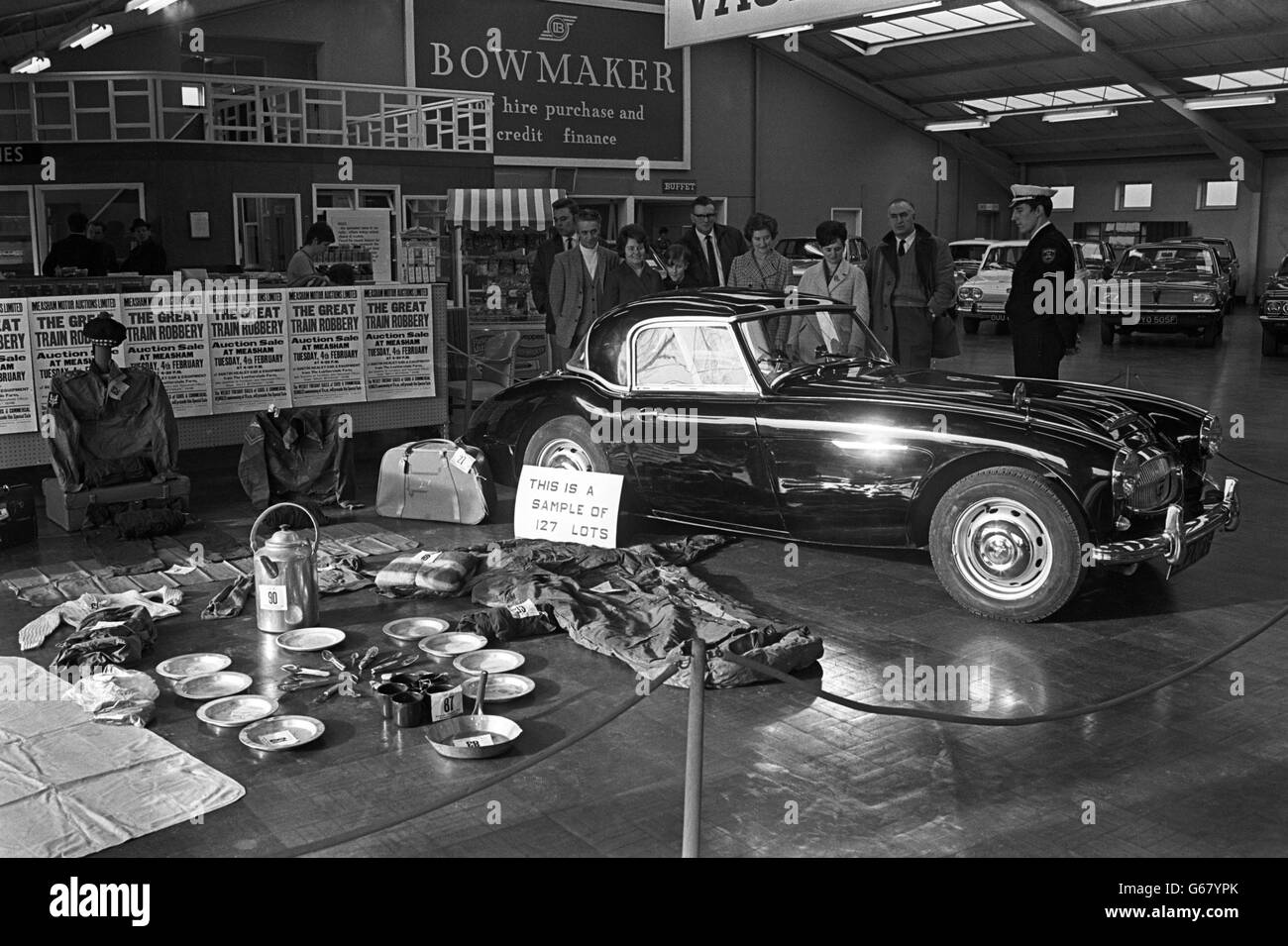 A security officer stands by as members of the public inspect a black Austin Healey car bought by Bruce Reynolds on 9 August, 1963, the day after the Great Train Robbery gang held up the mail train near Cheddington, Buckinghamshire. The car was found at the Leatherslade farm hideout and is to be auctioned at Measham, Leicestershire. The proceeds from the sale will go to a firm of loss adjusters representing the banks. Stock Photo