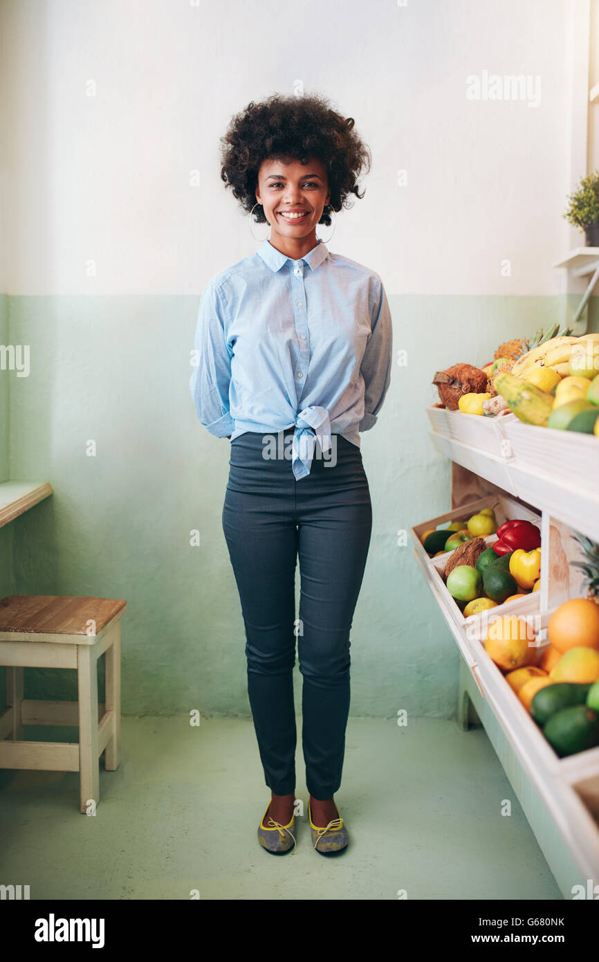 Full length portrait of happy young african woman standing in a juice bar. Female fruit juice bar owner. Stock Photo