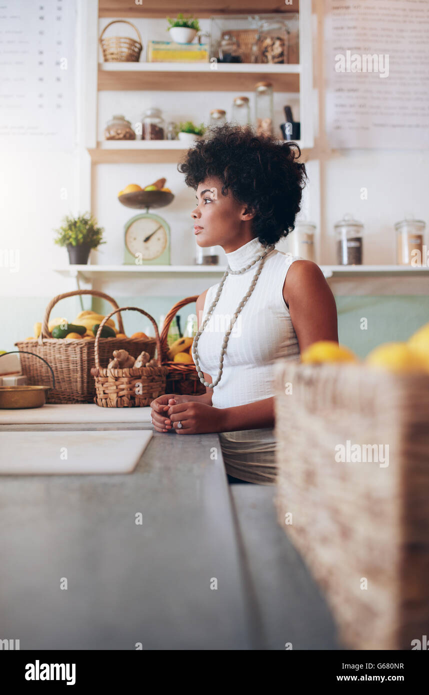 Side portrait of young woman employee standing at juice bar counter. African female fruit juice bar owner. Stock Photo
