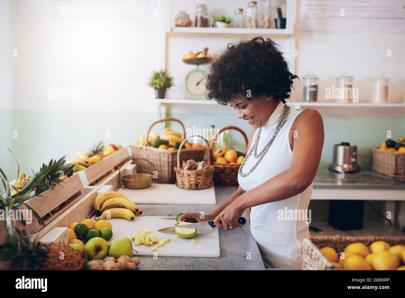 Shot of young african woman working at juice bar and cutting fruits. Female bartender making fresh juice. Stock Photo