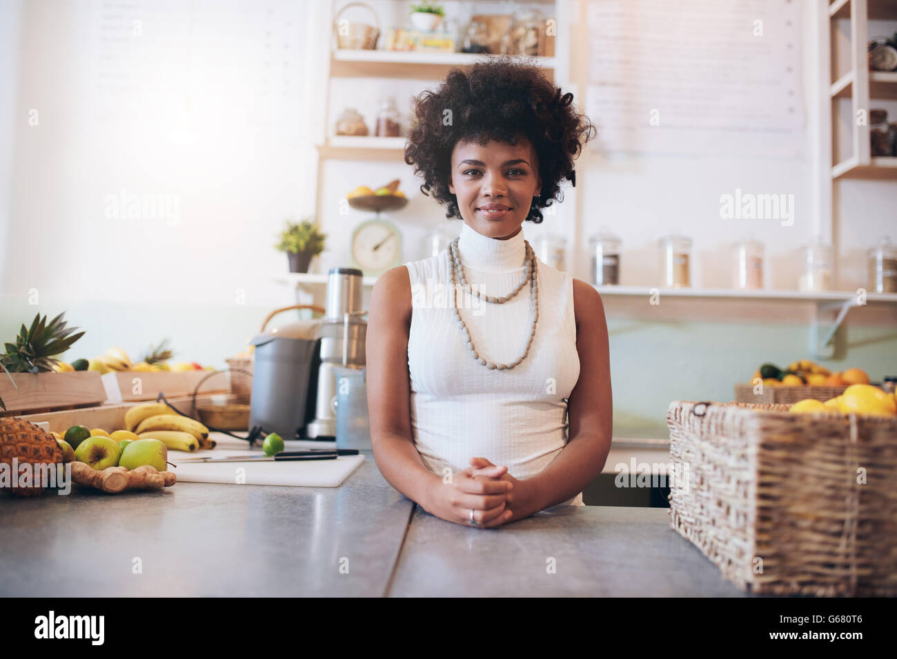 Portrait of attractive young woman working at juice bar, she is standing behind counter looking at camera. Stock Photo