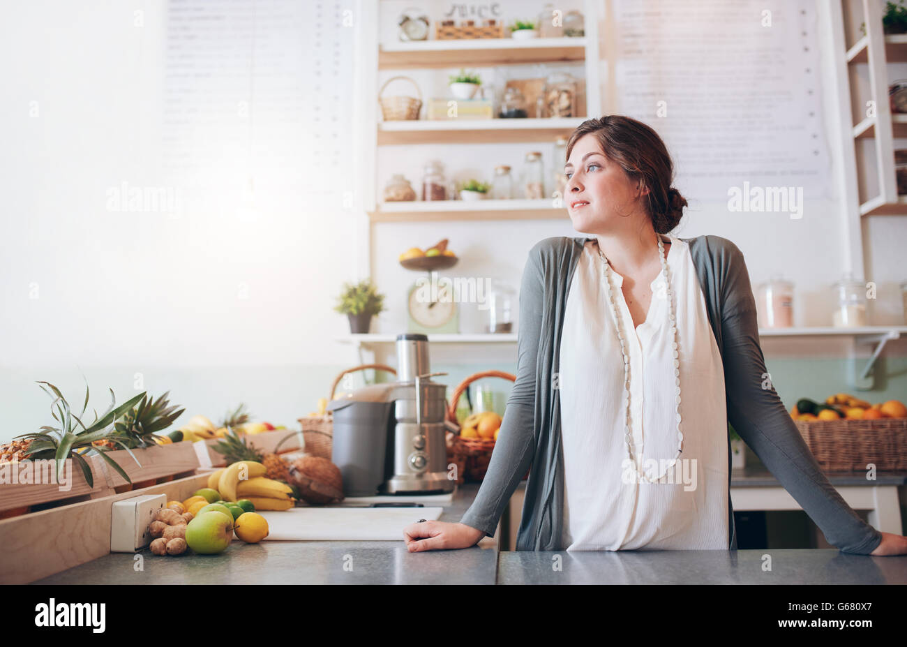 Portrait of attractive young woman standing behind the counter and looking away. Caucasian fruit juice bar owner looking at copy Stock Photo