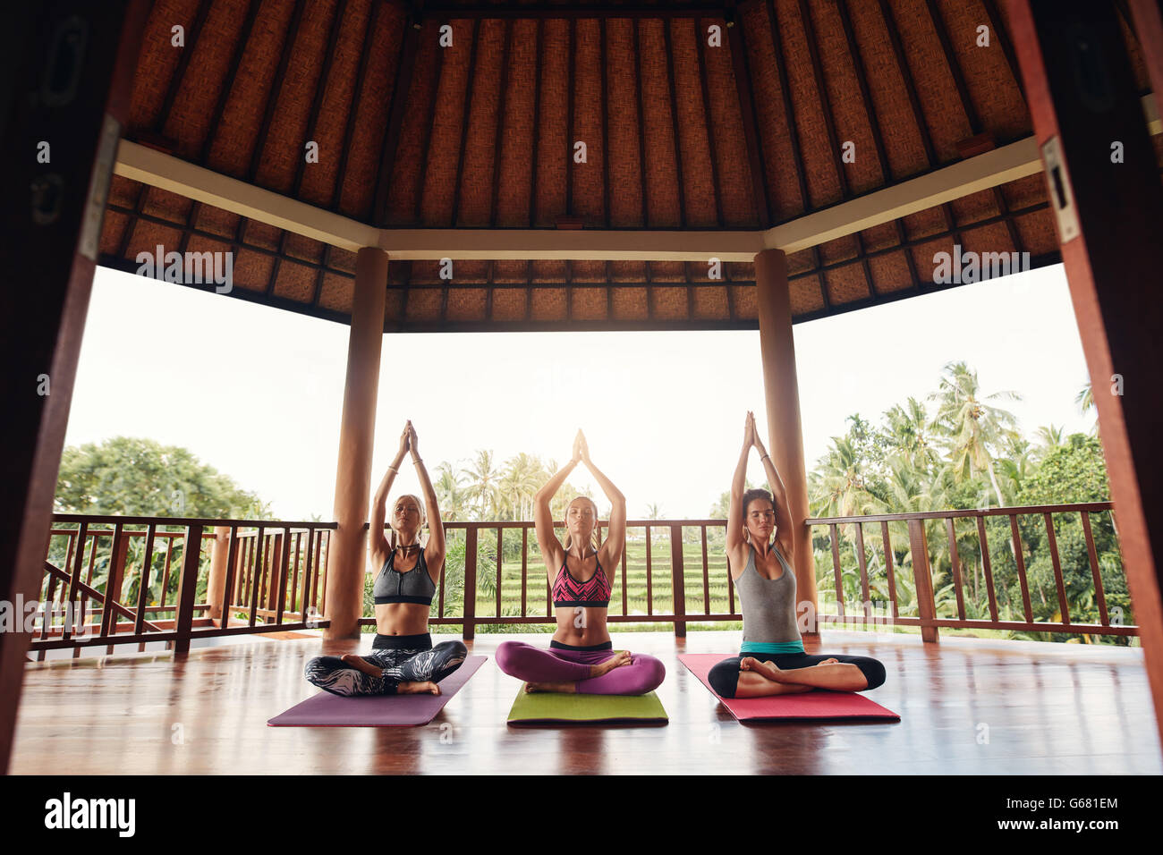 Three young women practicing yoga in a gym sitting cross legged on their mats and meditating. Group of people doing meditation i Stock Photo