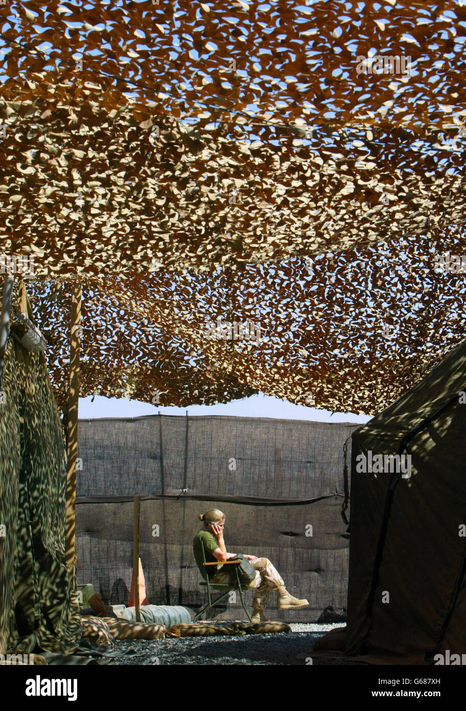 A Royal Air Force female officer makes a telephone call outside camoflague netting used as a shelter from the sun in Kuwait. British Royal Air Force personnel are now able to phone home free for 20 minutes a week. Stock Photo
