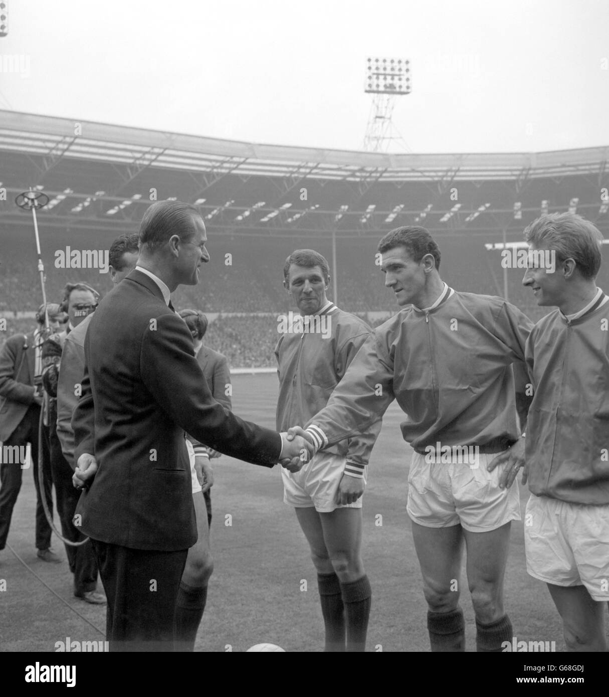 Prince Philip, The Duke of Edinburgh, shakes hands with centre-half Bill Foulkes as the Manchester United players were presented to him on the field at Wembley Stadium, London, before the kick-off in the FA Cup. On left is centre-forward David Herd, who was to score two goals, and on right is inside-left Denis Law, who was to score one goal in United's 3-1 victory over Leicester City. Stock Photo