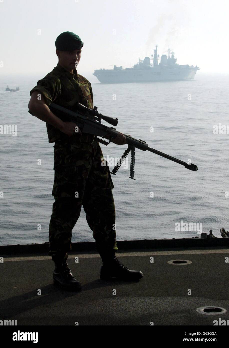 A Royal Marine from 40 Commando stands on the deck of British helicopter carrier HMS Ocean, with the HMS Ark Royal in the background, as they travel through the Persian Gulf. Stock Photo
