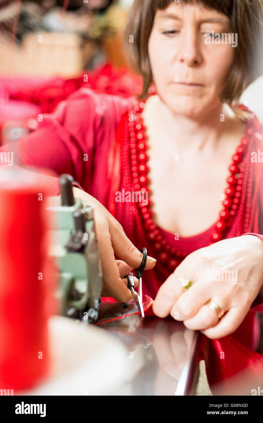 Seamstress in red dress and necklaces trimming cloth with scissors