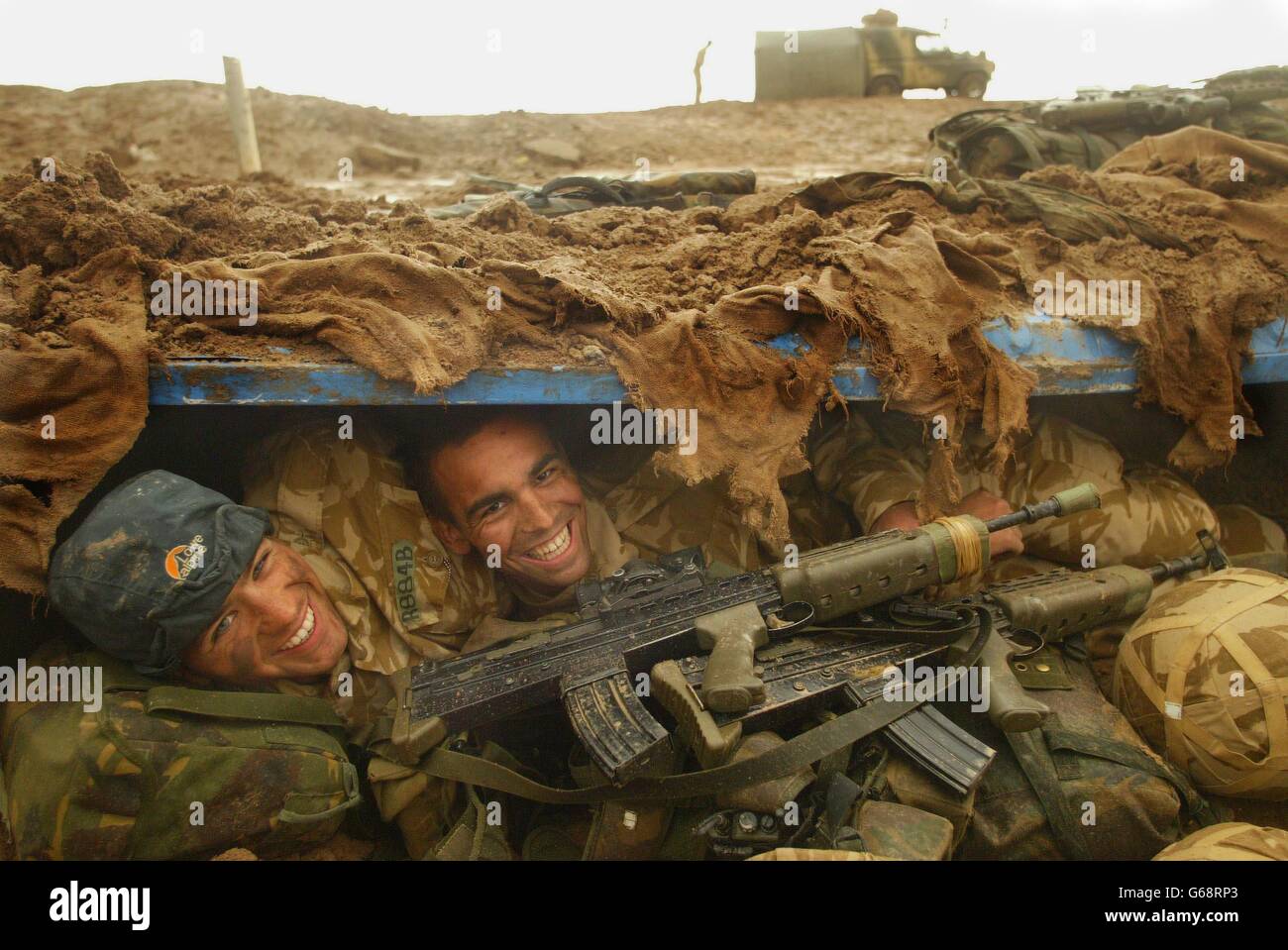 Members of 40 Commando Royal Marines dug in north of the Al Faw Peninsula, aproaching Basra, after heavy rainstorms in the desert, Marine Omar Rawlings, 20, (left) and Marine Delme King, 24, shelter in their fox hole. Stock Photo