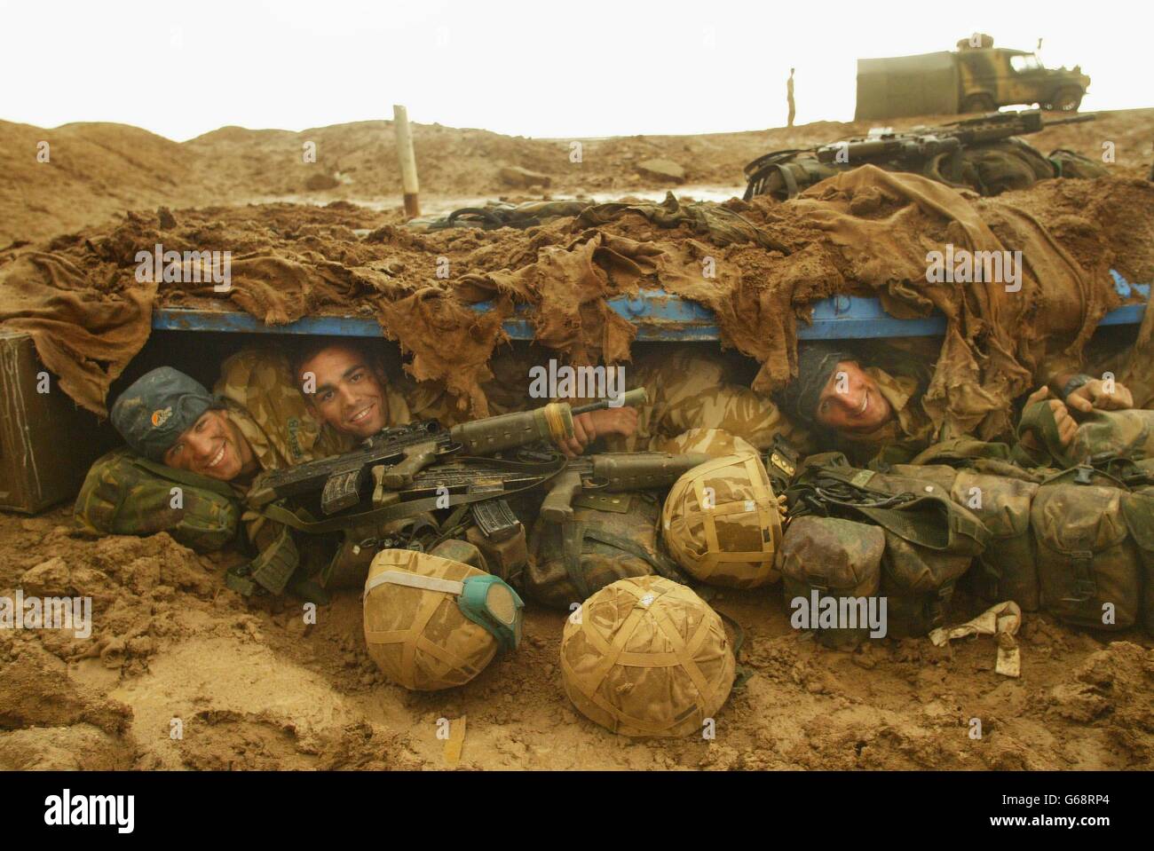 Members of 40 Commando Royal Marines dug in north of the Al Faw Peninsula, aproaching Basra, after heavy rainstorms in the desert, Marine Omar Rawlings, 20, (left) Marine Delme King, 24, and Jim Morton shelter in their fox hole. Stock Photo