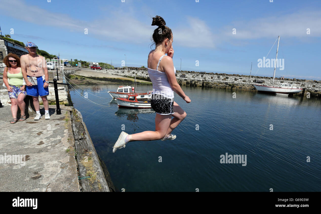 Teenagers jump into the harbour at Carnlough in Co Antrim, as the summer heatwave continues across the UK. Stock Photo