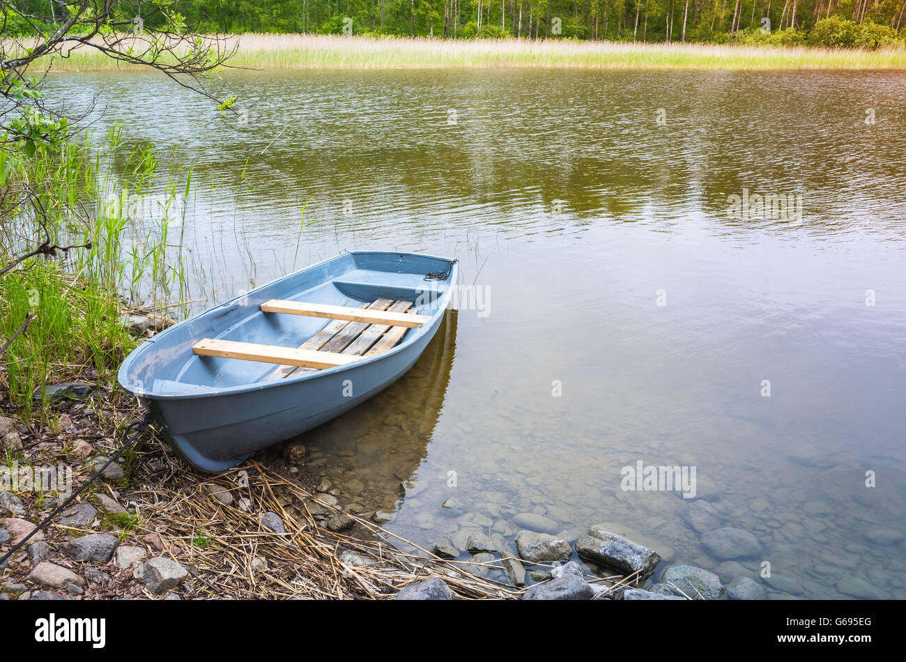 Small blue rowboat lays on coast of still lake Stock Photo