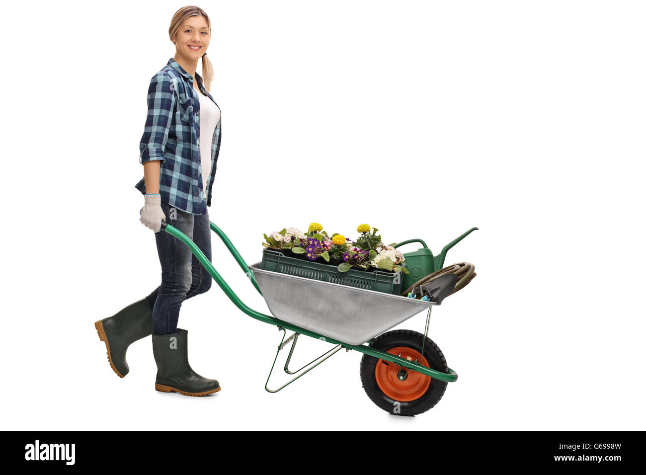 Full length portrait of a young woman pushing a wheelbarrow with gardening equipment isolated on white background Stock Photo