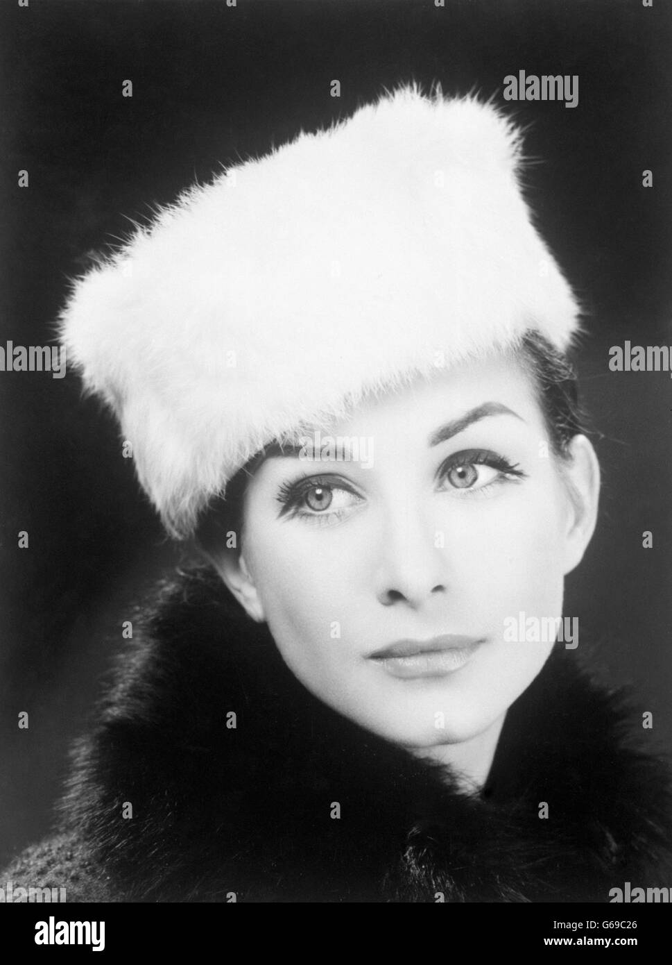 A model wears a white fur pillbox hat, named the Snowqueen. The crown of the hat is topped with white velvet. Stock Photo