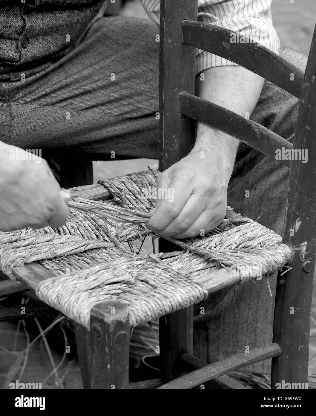 old man mender of chairs while repairing an old wooden chair with straw