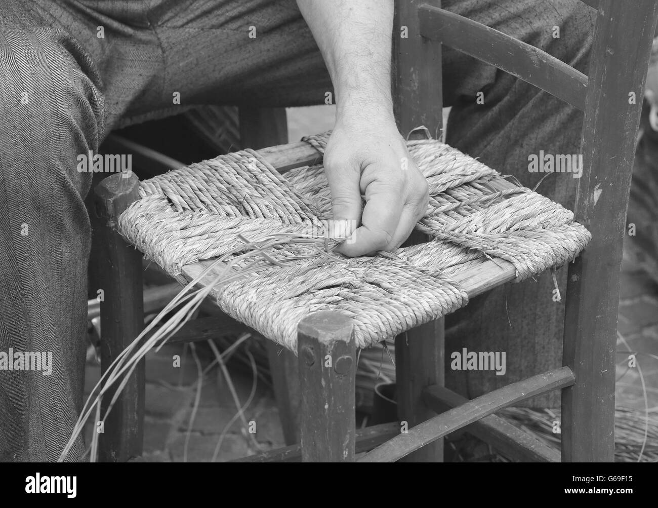 hands of a mender of chairs while repairing an old chair with straw Stock Photo