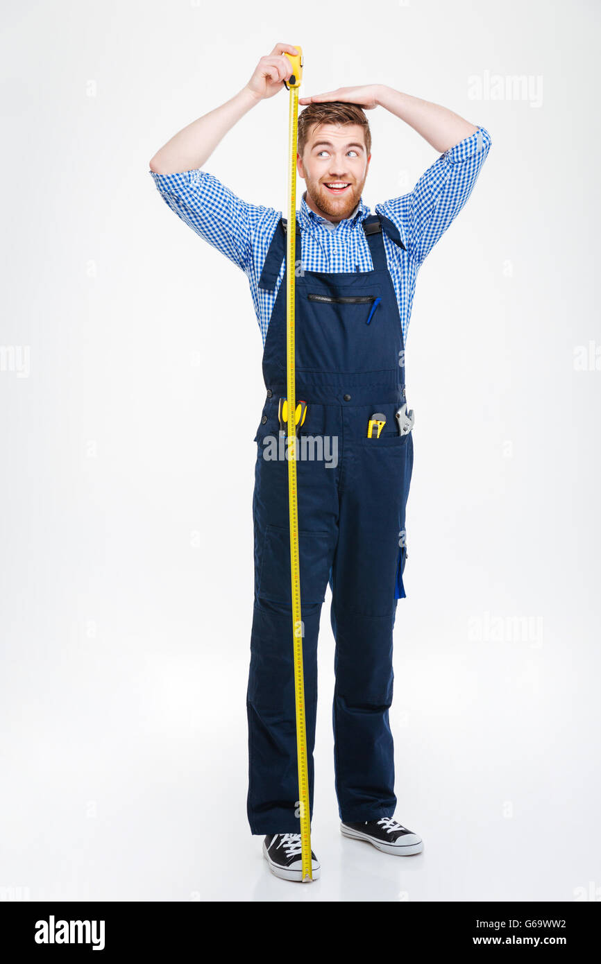 Happy funny young man in overall measuring his body height using tape Stock Photo