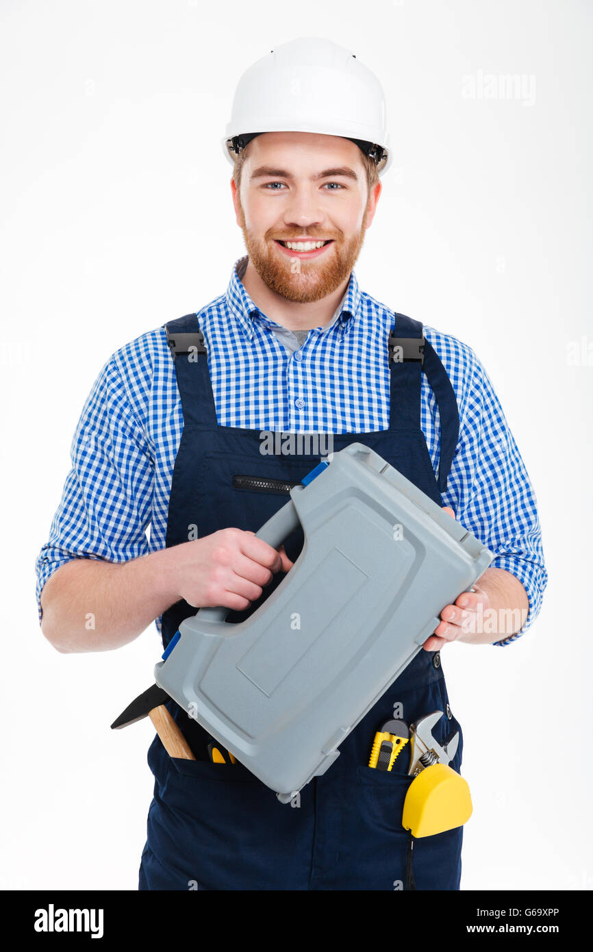 Smiling bearded young worker in helmet holding tool box Stock Photo
