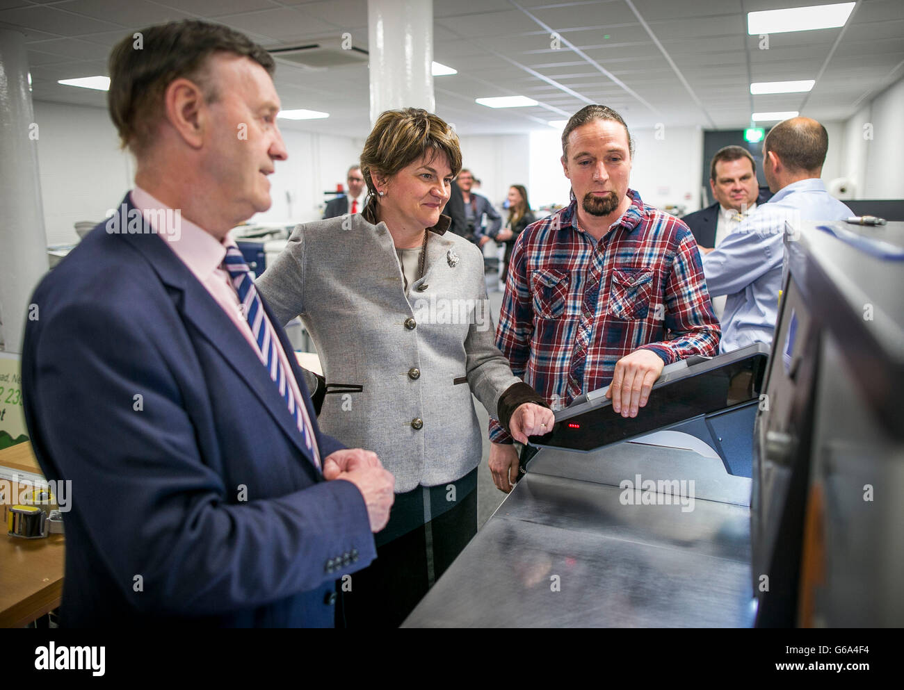 First Minster of Northern Ireland Arlene Foster is shown the workspace of Belfast based printing facility Media Design and Print, by owner Harry Beckinsale as lead print finisher Colin Mulholland (right) demonstrates a piece of new equipment during the official opening of the office space. Stock Photo