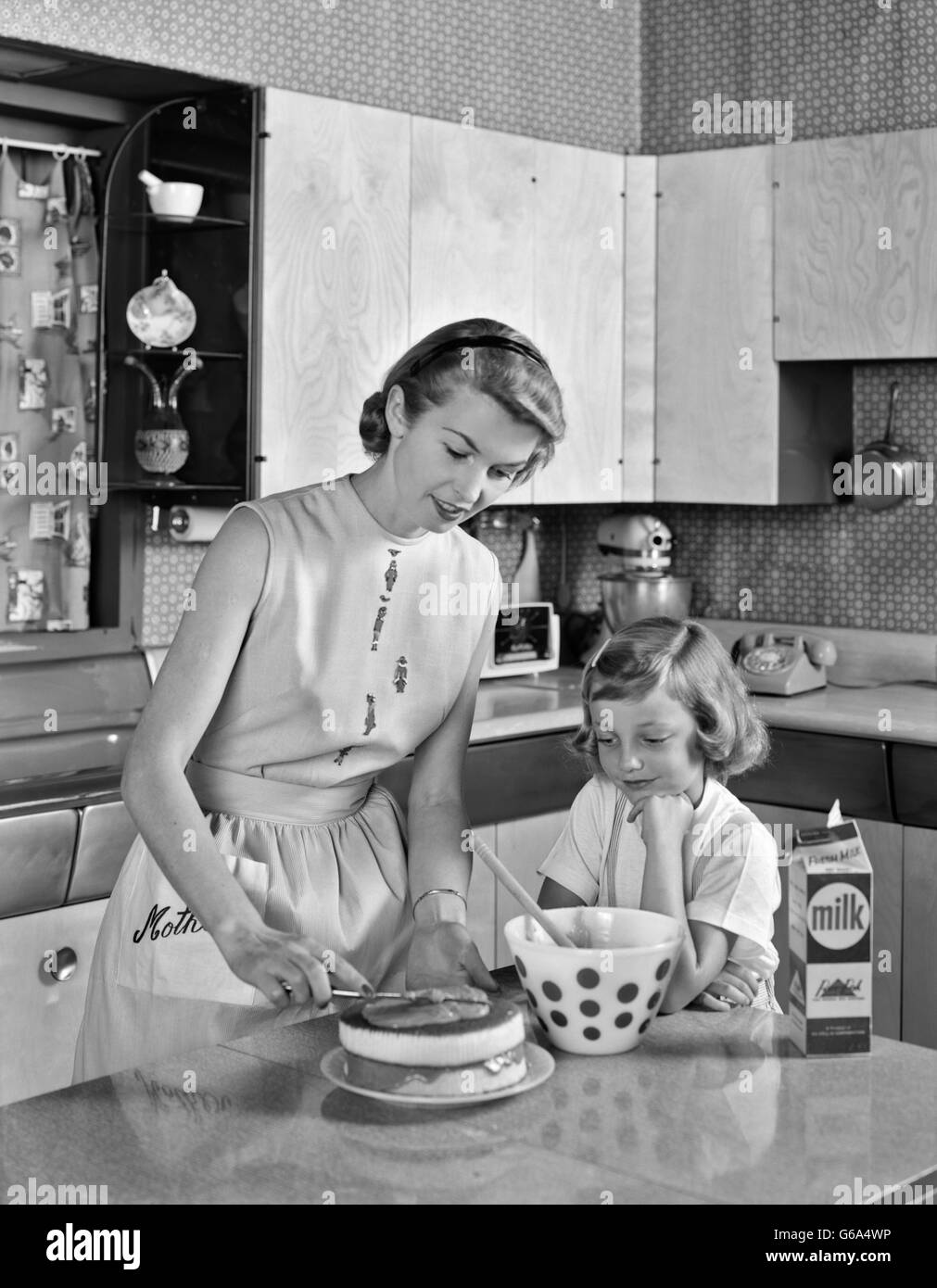 1950s MOTHER AND DAUGHTER IN KITCHEN FROSTING DOUBLE LAYER CAKE Stock Photo