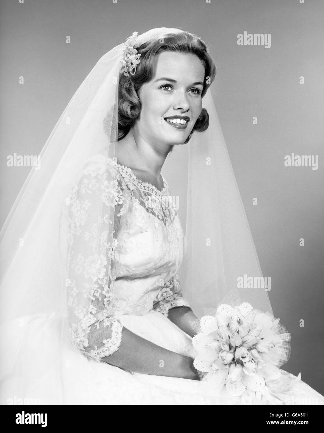 1960s PORTRAIT SMILING WOMAN BRIDE LACE DRESS NET VEIL HOLDING BRIDAL BOUQUET Stock Photo