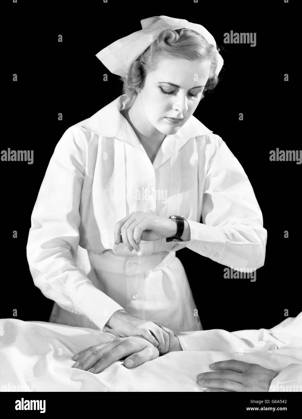 1930s FEMALE NURSE CHECKING PATIENT’S PULSE Stock Photo