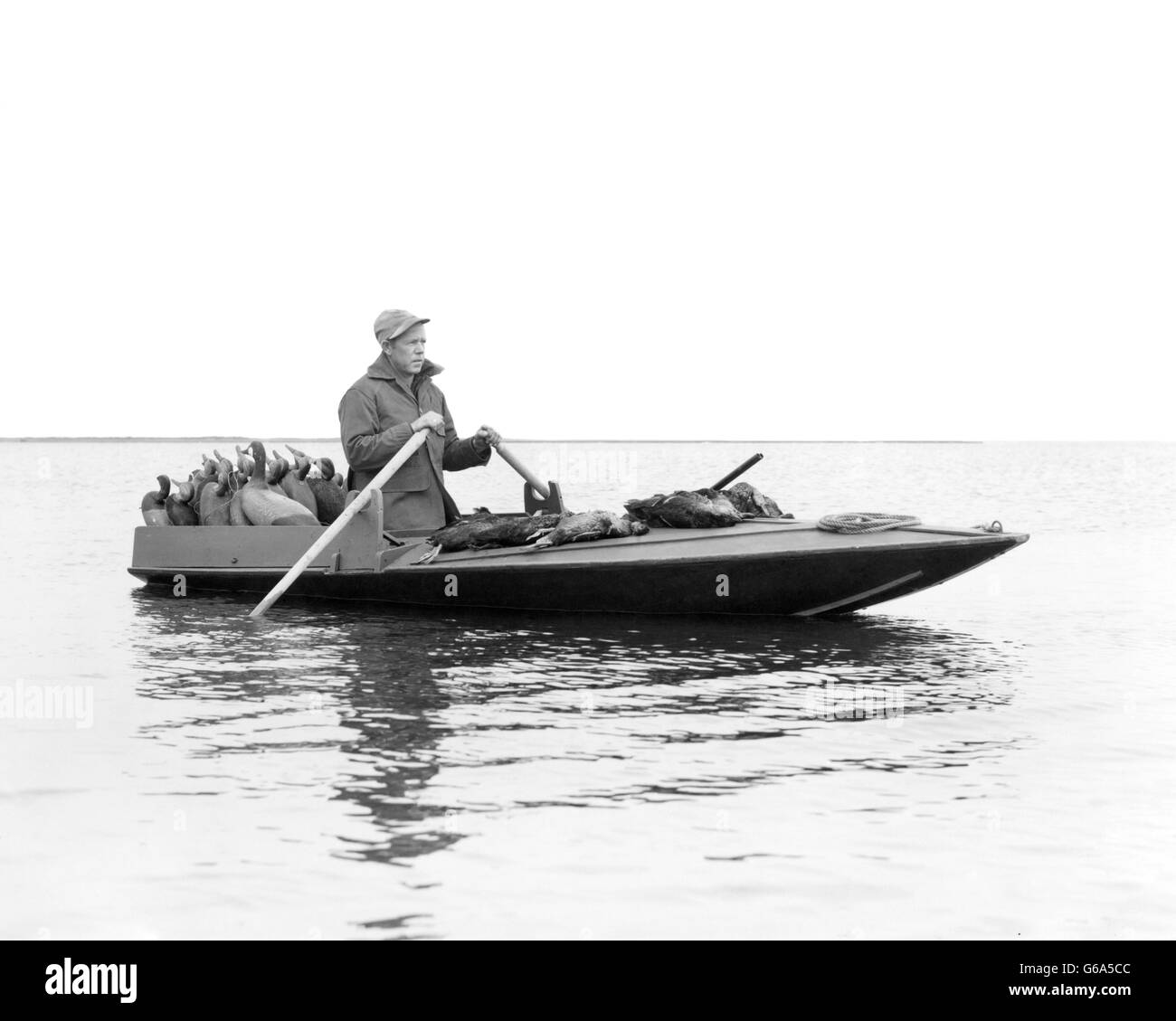 1950s MAN DUCK HUNTER ROWING DUCK BOAT DECOYS ON REAR DECK AND KILLED DUCKS ON FRONT BARNEGAT BAY NJ USA Stock Photo