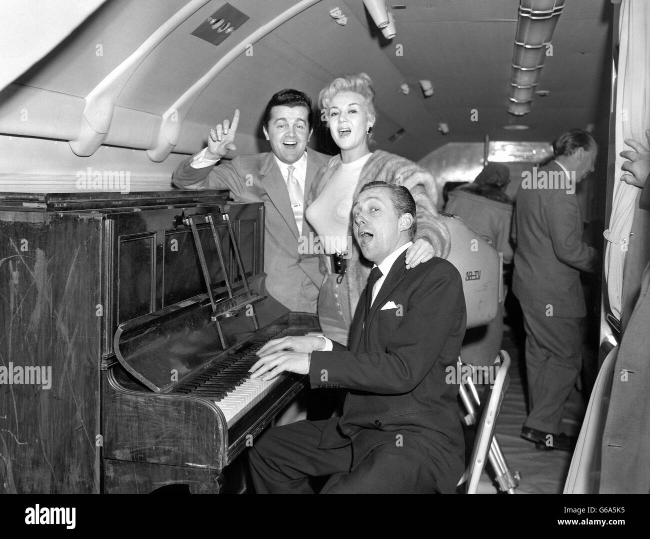 Hughie Green sits as the piano and is joined in a song by Ronnie Ronalde and Rosalina Neri aboard a BOAC Bristol Type 175 Britannia at London airport. They were rehearsing for a flight to New York which will be filmed as 'Jack Hylton's Monday Show' for screening on ITV. Stock Photo