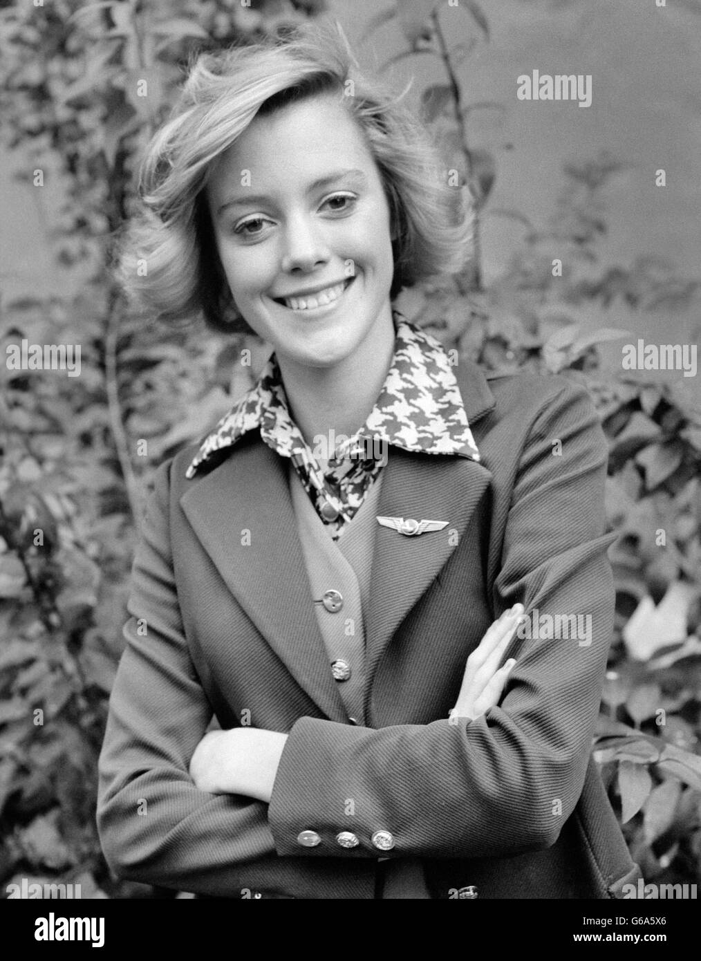 1970s PORTRAIT SMILING AIRLINE FLIGHT ATTENDANT WEARING WING PIN ON LAPEL STEWARDESS LOOKING AT CAMERA Stock Photo