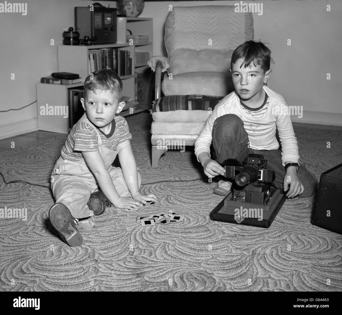 1940s 1950s TWO BOYS SITTING ON LIVING ROOM FLOOR VIEWING SLIDES WITH SLIDE PROJECTOR Stock Photo