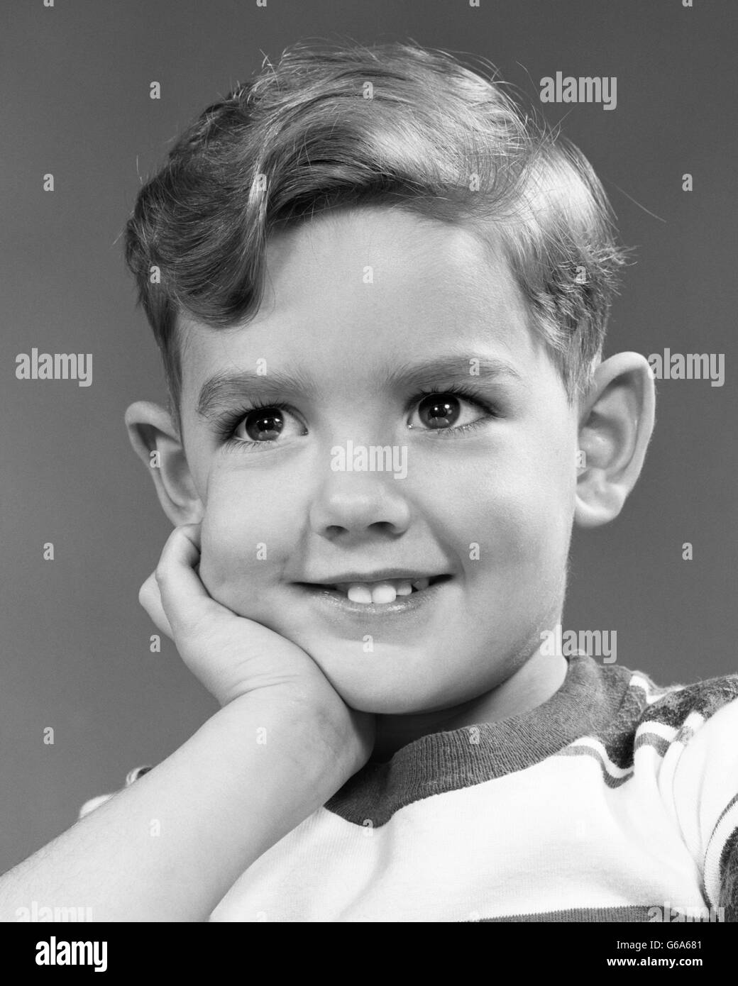 1950s PORTRAIT SMILING BOY LOOKING AT CAMERA FACE RESTING IN HAND Stock Photo