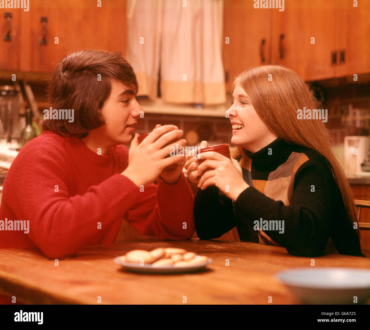 1970 1970s YOUNG TEENAGE TEEN COUPLE EAT COOKIE COOKIES DRINK BOY GIRL BOYS GIRLS DATE DATING FRIEND FRIENDS KITCHEN TABLE Stock Photo