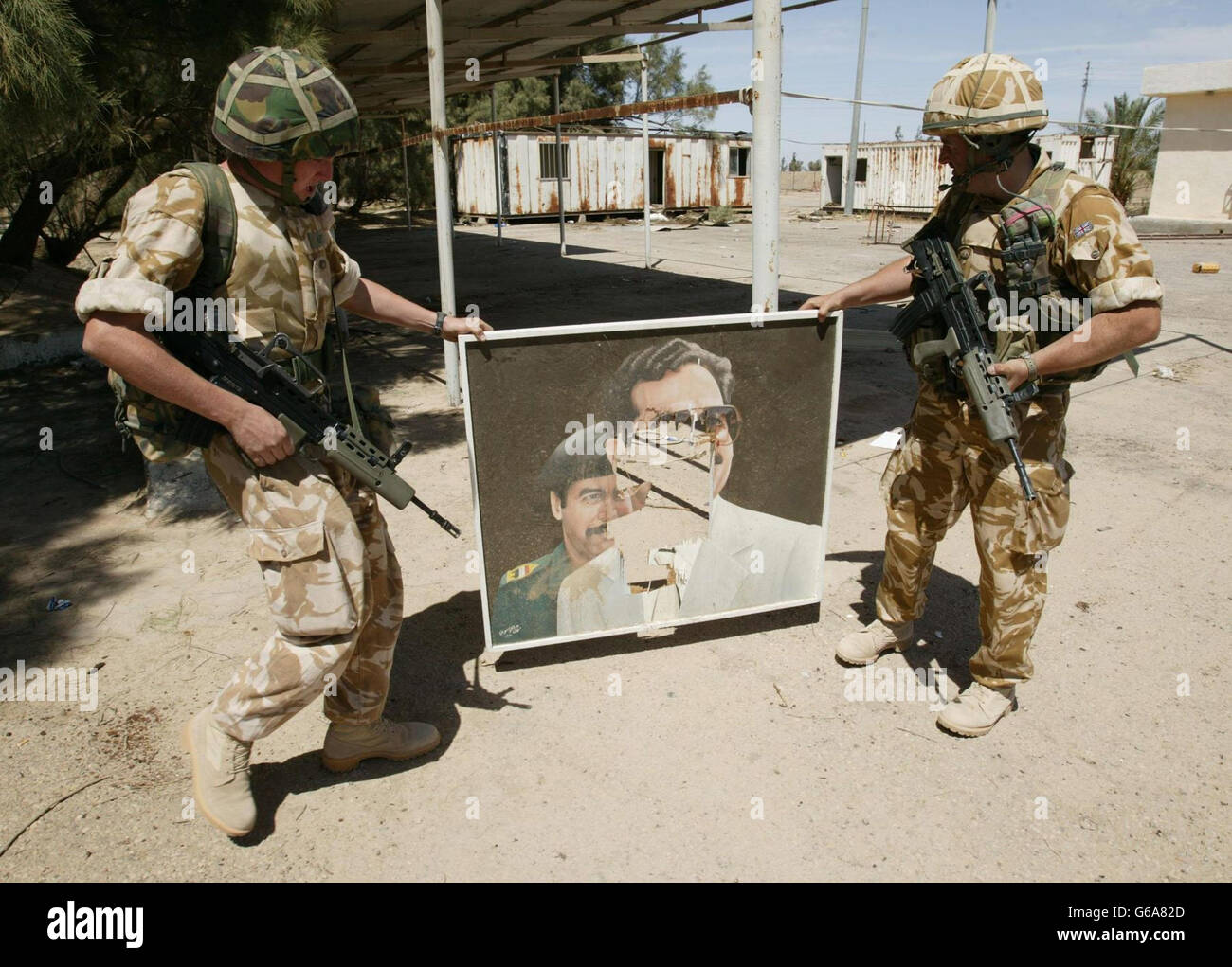 Soldiers from 2CS regiment RLC carrying a defaced portrait found in the grounds of the mansion of Saddam Hussain's cousin, Ali Hassan Al Majid, also known as 'Chemical Ali', after local people looted the house near Basra. PA Photo: Dan Chung/The Guardian/MOD Pool. Stock Photo