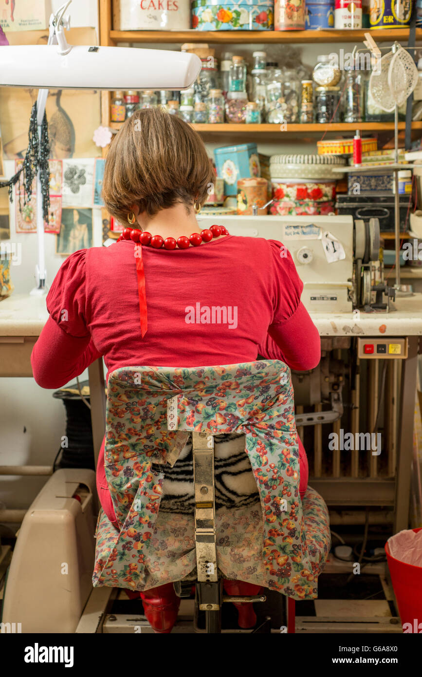 A seamstress in red seated, back turned, and working by a sewing machine Stock Photo