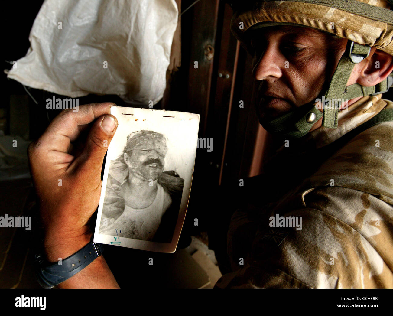NOTE GRAPHIC CONTENT. A soldier holds up a photo showing the dead body of what is thought to be an Iraqi, discovered along with human remains and coffins at an abandoned Iraqi base near Basra. Hundreds of human remains were discovered in a makeshift morgue. Dan Chung / Guardian / MOD Pool. *... by British soldiers in southern Iraq. The skulls, bundles of bone in strips of military uniform, were dumped in plastic bags and unsealed hardboard coffins in an abandoned Iraqi military base on the outskirts of Al Zubayr. It was impossible to say how long the remains had lain there but the grim Stock Photo