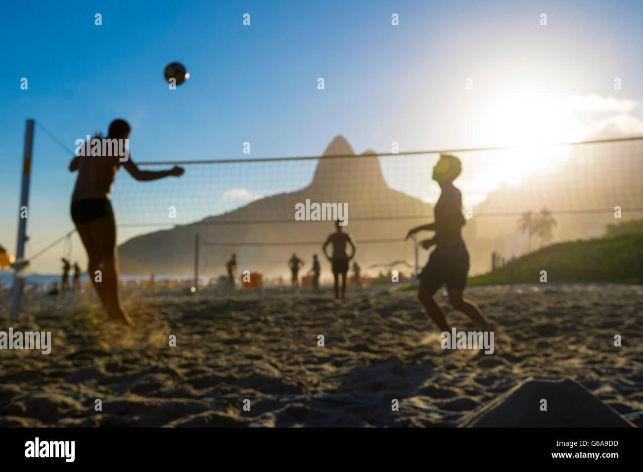 Defocused scene of silhouettes of Brazilians playing futevolei (footvolley) against a sunset backdrop of Two Brothers Mountain. Stock Photo