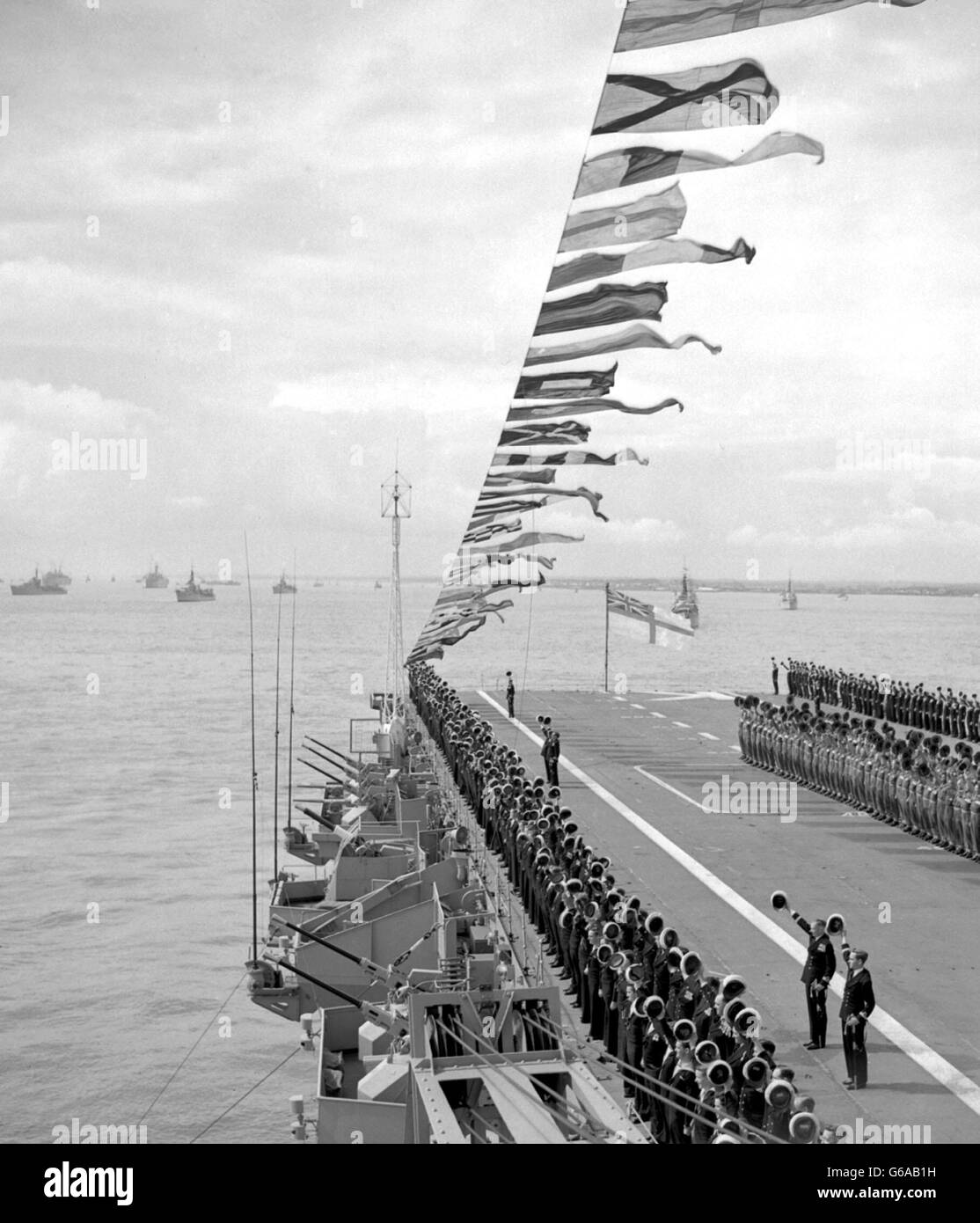 Crew of the Australian aircraft carrier Sydney line up on the ship's flight deck to give three cheers for the Queen during the Coronation Naval Review at Spithead. The Queen, aboard the Royal yacht, the dispatch vessel Surprise, passed down the lines of British, Commonwealth and Foreign warships. Stock Photo