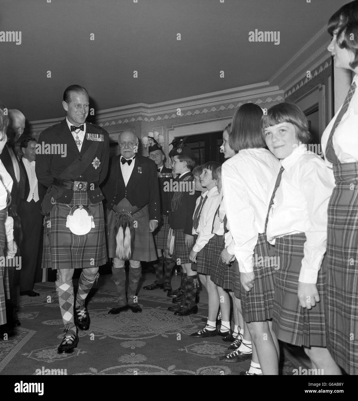 Prince Philip, The Duke of Edinburgh, wearing the kilt, smiles at children of the Royal Caledonian Schools who formed a guard of honor when he arrived to take the chair at the schools' 150th anniversary dinner. Behind his Royal Highness is Sir Edward Reid, chairman of the governors of the schools Stock Photo