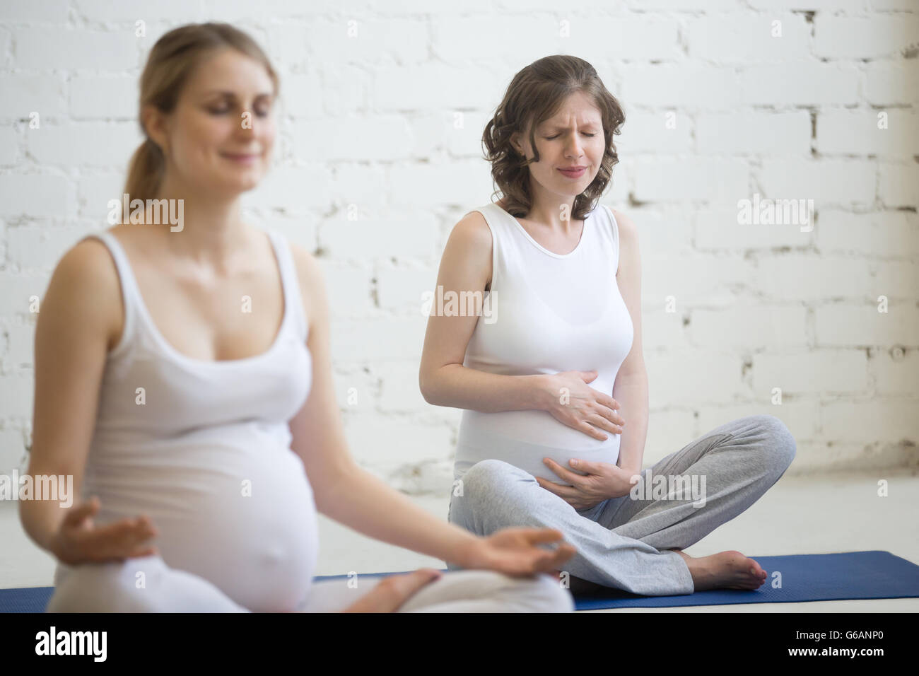 Pregnant person feeling belly pain during fitness or yoga class indoors. Young pregnant woman holding her stomach feeling unwell Stock Photo