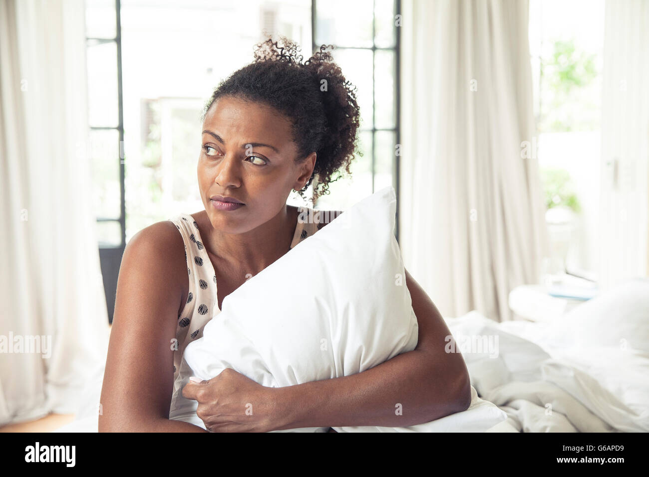 Woman hugging pillow on bed, portrait Stock Photo