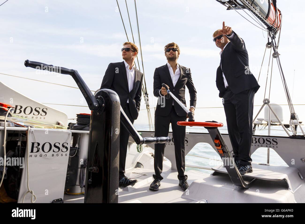 Actor Douglas Booth pictured at the tiller before the Artemis Challenge at Aberdeen Asset Management Cowes Week where he sailed onboard the Open 60 racing yacht, Hugo Boss, with round the world yachtsman Alex Thomson (right) and fellow actor Sam Reid (left). Stock Photo