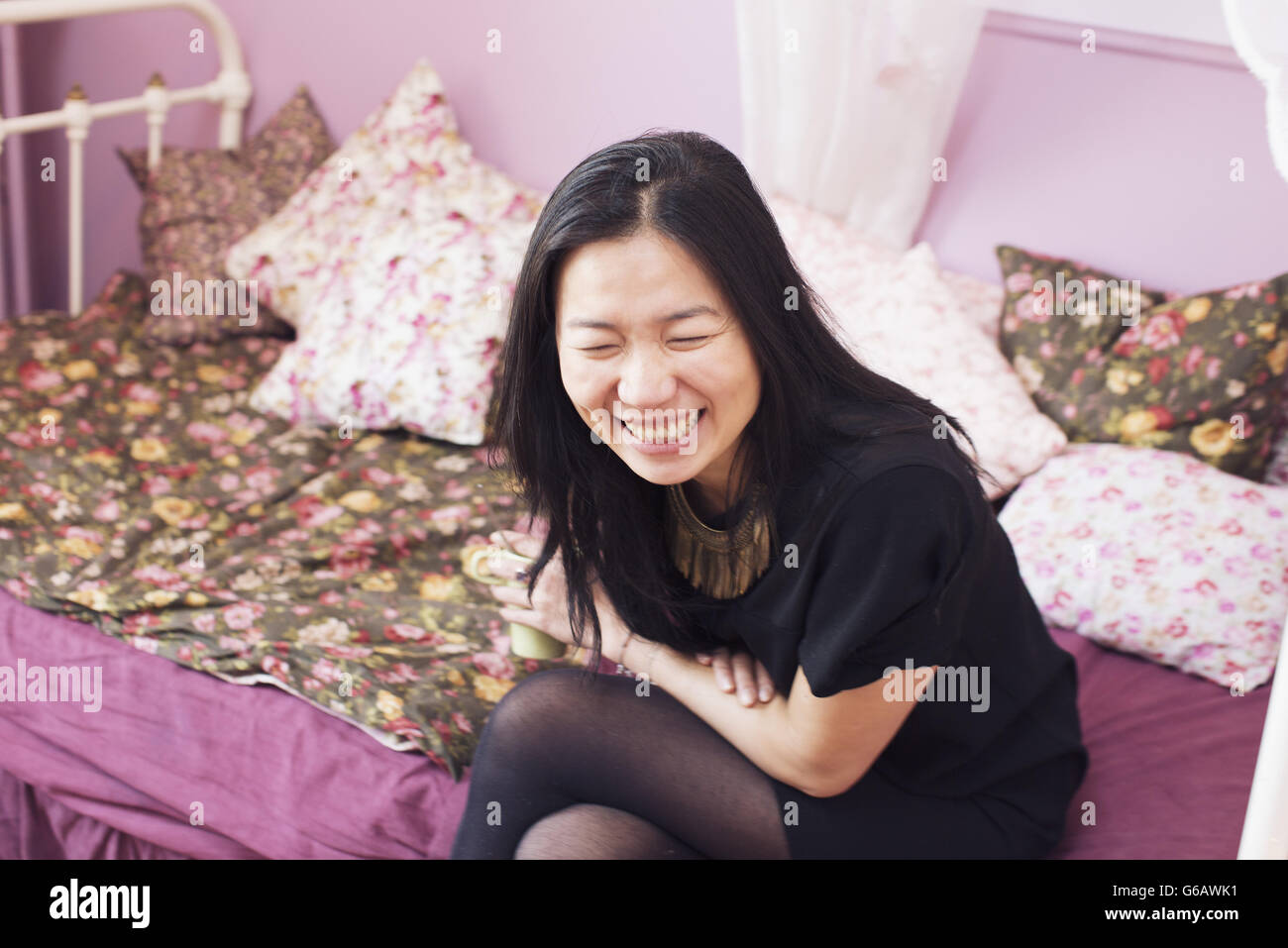 Woman sitting on bed laughing Stock Photo