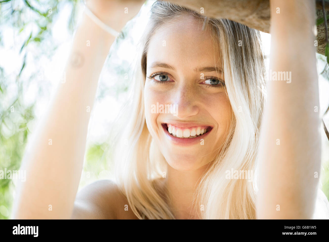 Young woman leaning against tree branch, smiling, portrait Stock Photo